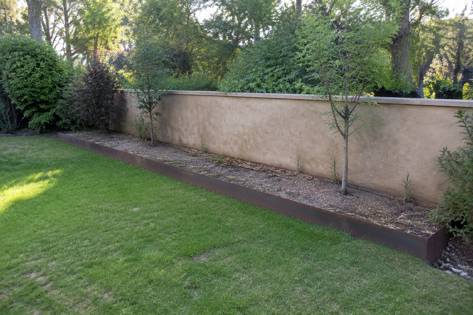 Jardinera lineal de acero corten antes de la intervención, con ramas secas y piedra deteriorada